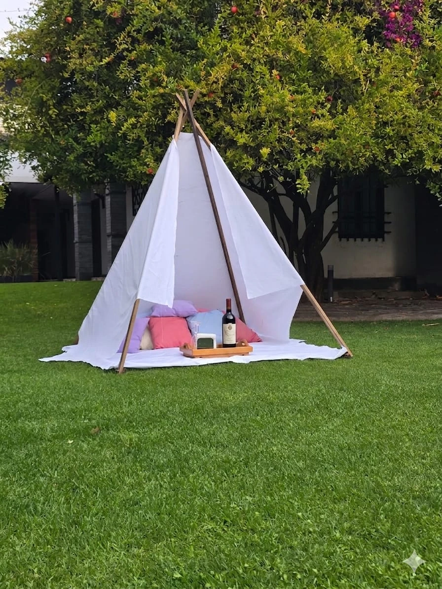 Teepee blanco en jardín con cojines y vino