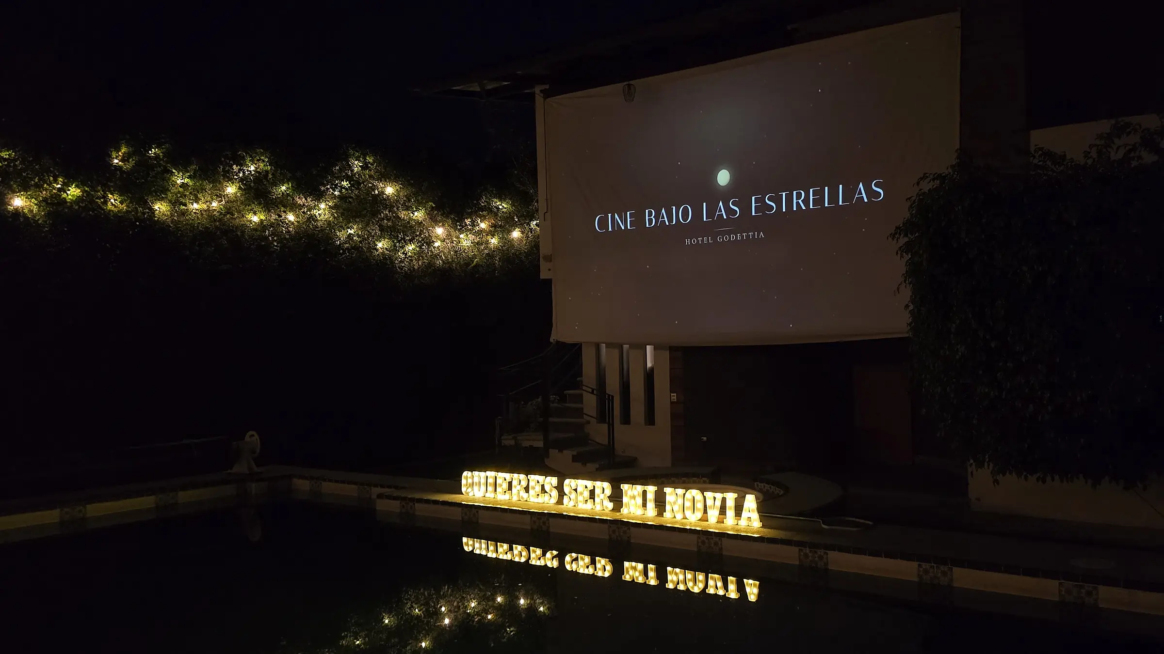 Las letras ¿Quieres ser mi novia? encendidas y reflejadas en la alberca, bajo la pantalla de Cine bajo las estrellas