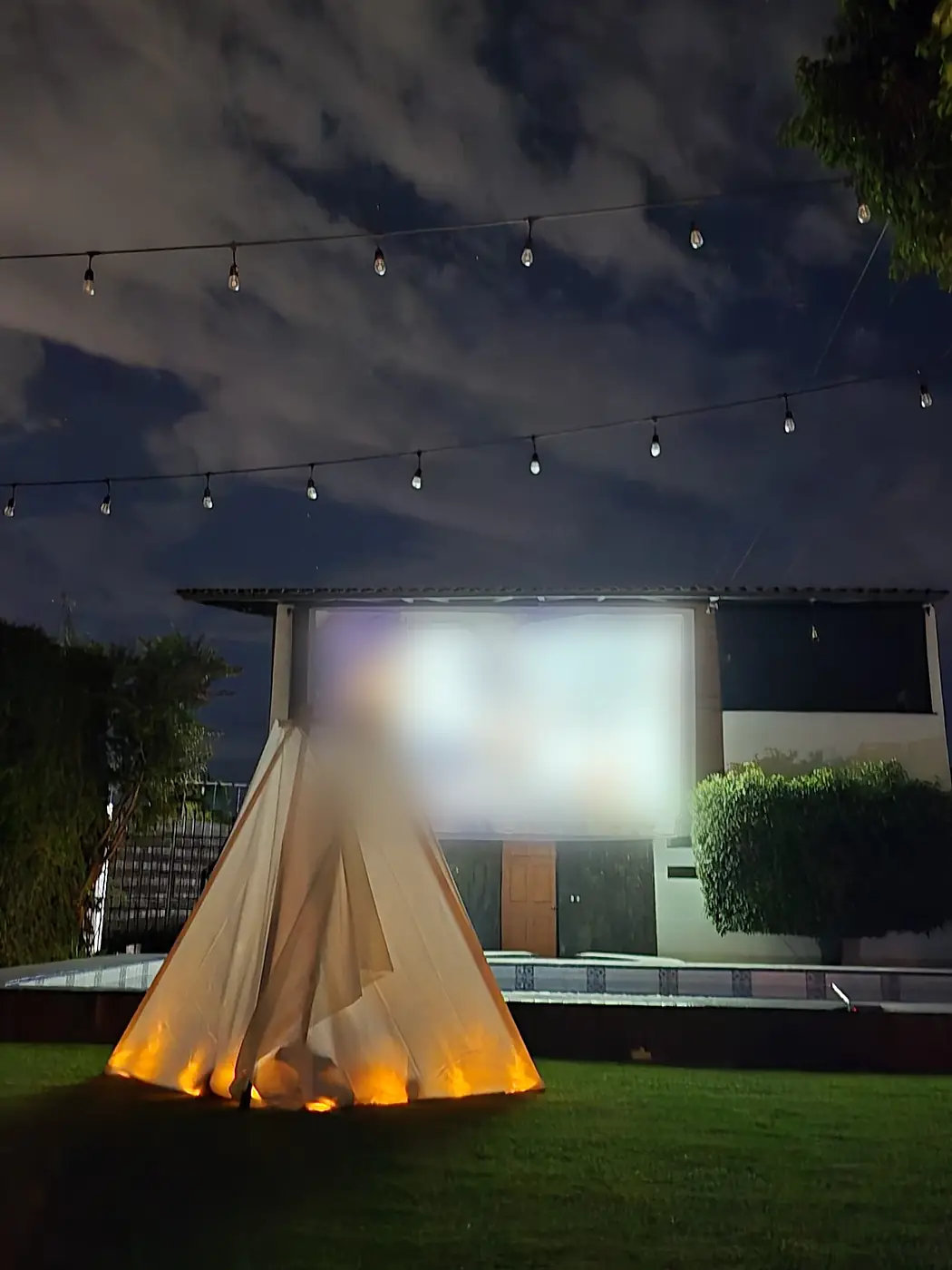 El teepee encendido por dentro frente a la pantalla, bajo un cielo con nubes