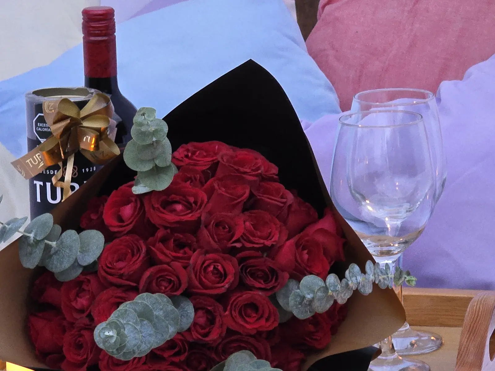 Ramo de rosas rojas, botella de vino y copas sobre los cojines del teepee